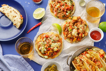 Overhead image of mexican tacos with chili con carne, sweet potatoes and grated cheese served over a blue background