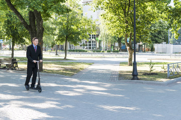 Businessman in suit goes on a kick scooter on a city park