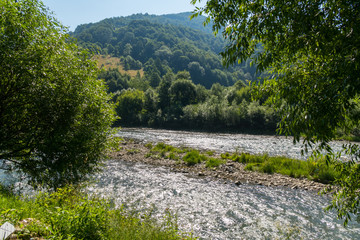 a beautiful landscape of mountainous terrain slopes covered with greenery, the river babbling leisurely on its business and a piece of blue sky in the distance