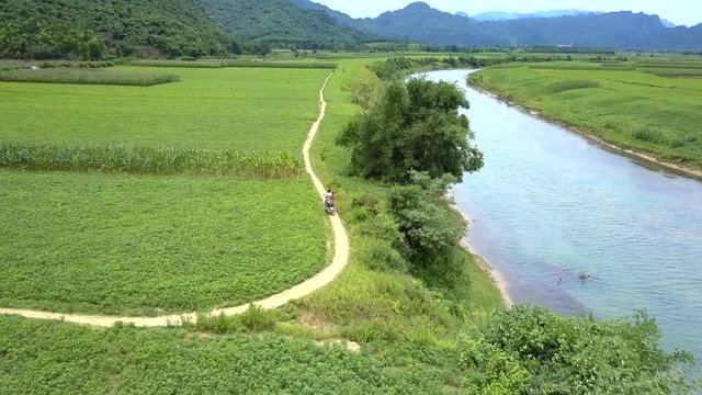 couple on scooter rides between river and peanut field