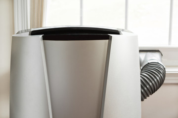 Portable air conditioner in front of brightly lit window.