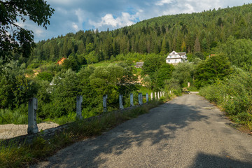 Road across the bridge across the river that leads to the village under a mountain with a forest