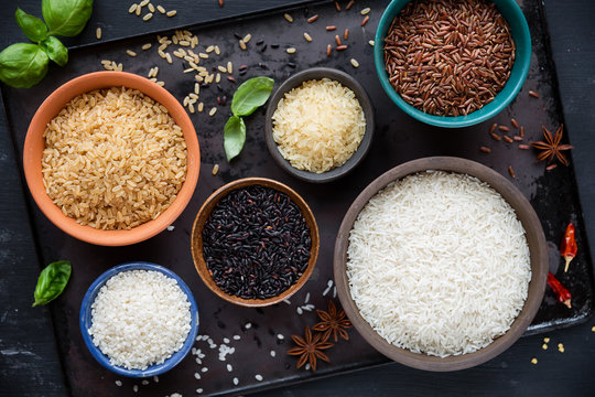 Variety of rice - red rice, black rice, basmati, whole grain rice, long grain parboiled rice and arborio rice - in bowls. Overhead view
