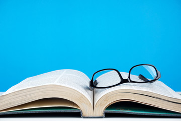 Education concept. An old book, eyeglasses over blue background