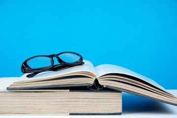 Education concept. An old book, eyeglasses over blue background