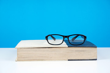 Education concept. An old book, eyeglasses over blue background