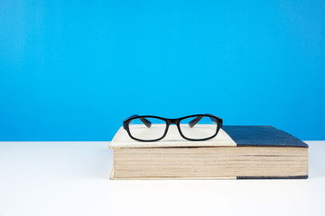 Education concept. An old book, eyeglasses over blue background