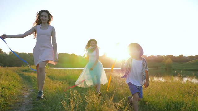 family pleasures, lovely girls with little boy in hat happily spend leisure with ribbons and toy windmills outdoors in sunlight at sunset