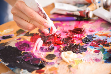 Closeup of paintbrush in woman hands mixing paints on palette