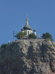 Domes with crosses of a beautiful church standing on a rock of stone with a fence on the edge and a blue cloudless sky above them.