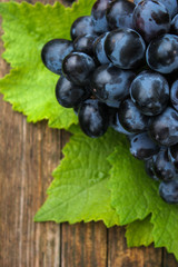 Blue grapes and bright grape leaves on an old wooden surface, close up.