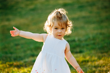 Cute little blonde girl in pink jacket, gray pants and rubber boots is jumping over a puddle on a rainy day