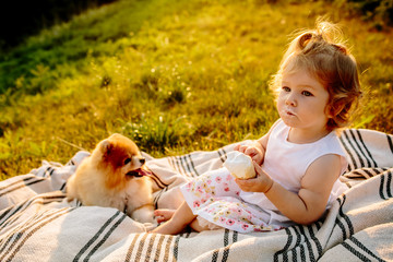 a little girl with ice cream sitting on a blanket in the Park at sunset. Dog looks at it