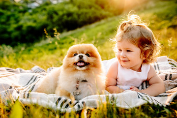 Little girl and pets. The girl and a dog lying on a blanket on a green park. Sunset time. Pedigree dogs Spitz. Funny animals. Outdoor picnic.
