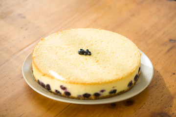 Blueberry Cheesecake with four blueberries in the middle, on a plate, on a  wooden table
