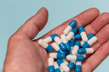 Hand holding drugs pills capsules on blue background