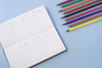 Calendar with multicolored pencils isolated on blue pastel background desk. Flat lay, space for text.