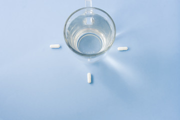 White pills organized around the fresh water on a pastel light blue table.