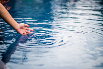 The hand that touches the blue water. The pool is clean and bright. With a drop of water on the water.