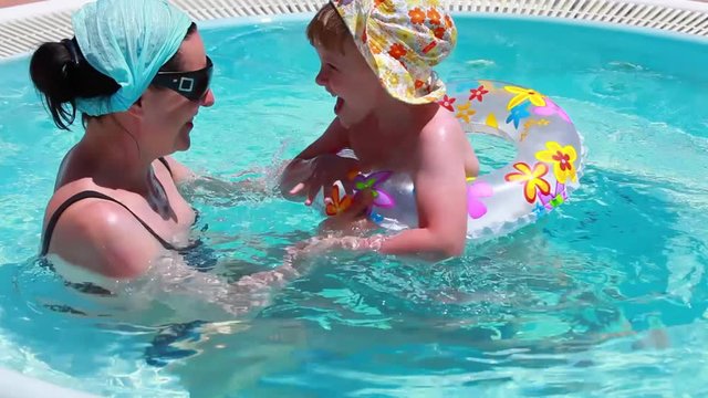 Mom teaches his little daughter to swim and play in the water on a swimming mug - the child and his mother are swimming in the pool with azure water together