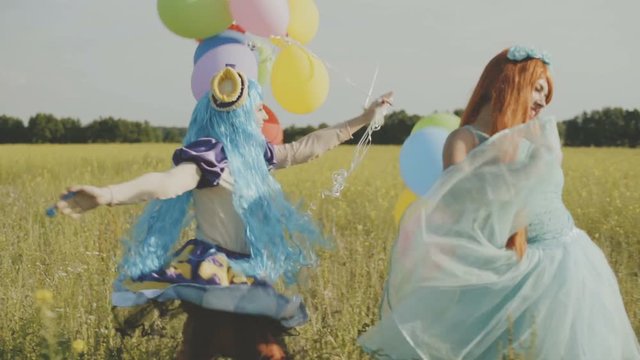 Two cheerful girls in bright costumes of princesses and with balloons are having fun in the field.
