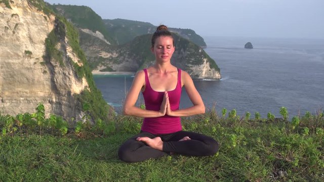 Meditating in lotus position, doing yoga in morning on cliff near ocean