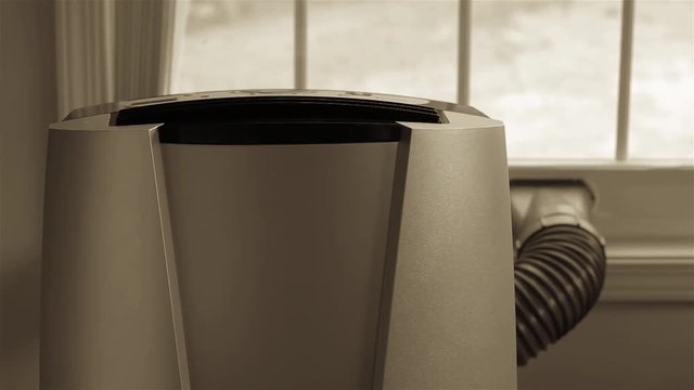 Footage of portable air conditioner in front of brightly lit window.