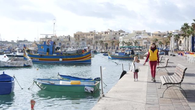 Mother with little child daughter walk the embankment of fishing village Marsaxlokk Malta