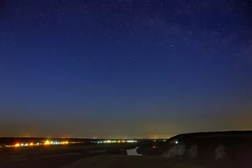 Foto op Canvas Sterren aan de nachtelijke hemel boven de riviervallei en de stad. De kosmische ruimte is gefotografeerd op een lange sluitertijd. © olgapkurguzova