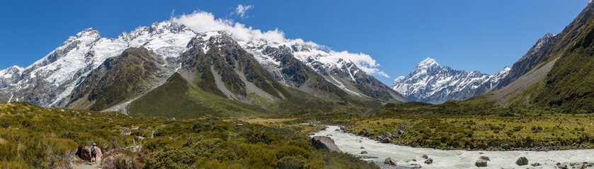 Panoramic view of a hiker walking towards Mount Cook beside a river in Aoraki Mount Cook national park, south island, New Zealand