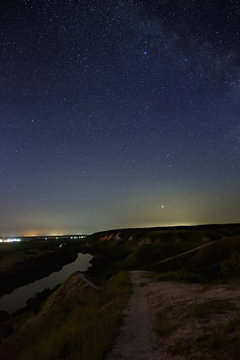 Stars in the night sky over the river valley and city. The cosmic space is photographed on a long exposure.
