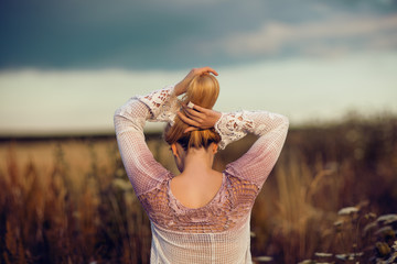 Beautiful blonde woman with long hair standing in a rural flower field outdoors, raising her hair,...