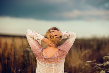 Beautiful blonde woman with long hair standing in a rural flower field outdoors, raising her hair,...