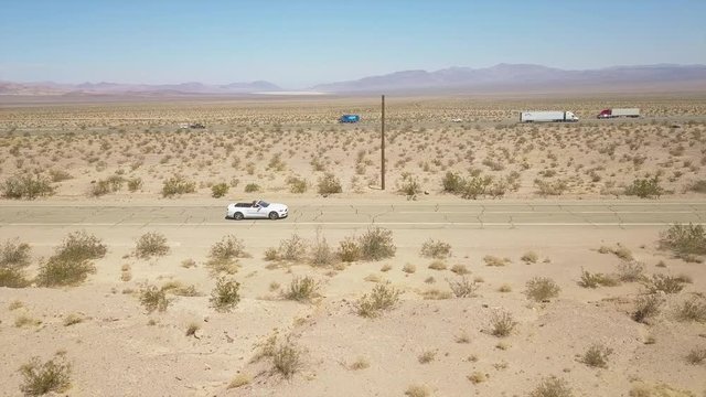 Side aerial view of a car driving on a road in the desert
