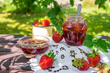 Strawberry jam and juicy ripe strawberries on a wooden table in the garden on a summer sunny afternoon in a rustic style, the concept of gardening, healthy organic vitamin nutrition