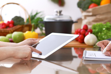 Closeup of human hands cooking in kitchen using touch pad. Women discuss a menu. Healthy meal, vegetarian food and lifestyle concept