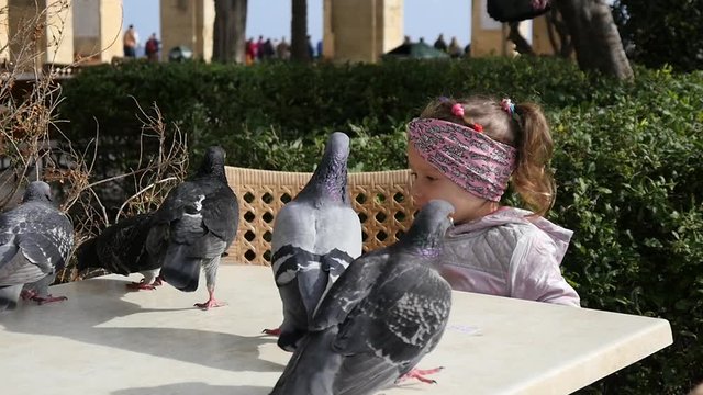 Valletta, Malta - Kid girl feeding street birds pigeons on a cafe table slow motion