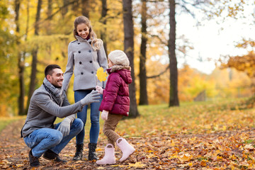 Fototapeta premium family, season and people concept - happy mother, father and little daughter with maple leaf at autumn park