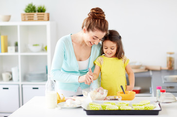 family, cooking, baking and people concept - happy mother and little daughter making batter for muffins at home kitchen