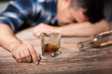 Fototapeta na wymiar alcoholism, alcohol addiction and people concept - male alcoholic with glass of whiskey and bottle lying or sleeping on table at night