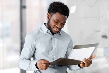 business, people and corporate concept - african american businessman with folder at office