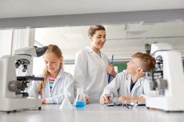 Fototapeta premium education, science and children concept - teacher and students studying chemistry at school laboratory and writing to workbooks