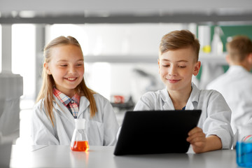 Fototapeta premium education, science and technology concept - kids with tablet pc computer studying chemistry at school laboratory