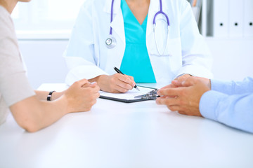 Doctor and family couple of patient are discussing something, just hands at the table. Medicine concept