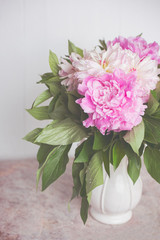 Delicate pink and white peonies in a white beautiful vase on a marble table