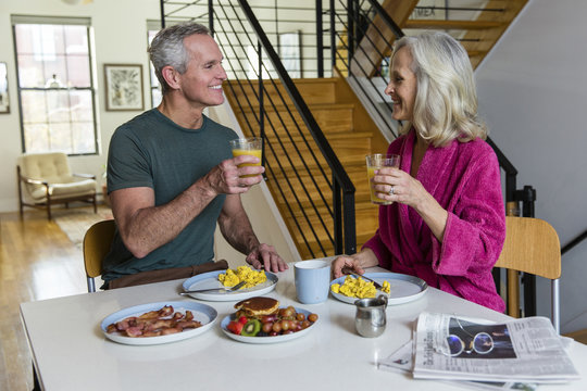 Smiling couple holding juices while looking each other face to face at dining table