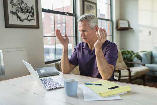 Shocked Mature Man Gesturing While Looking At Laptop Computer On Table In Living Room