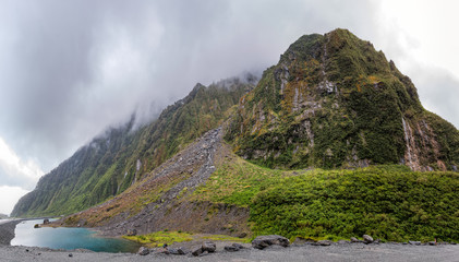 Obraz premium Rockface with waterfalls and a small lake near Fox Glacier on New Zealand's south island.