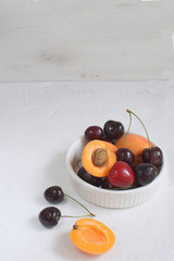 Apricots and cherries in white porcelain bowl Summer fruit and berries concept Harvesting Organic fruits White background Copy space