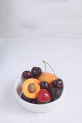Apricots and cherries in white porcelain bowl Summer fruit and berries concept Harvesting Organic fruits White background Copy space
